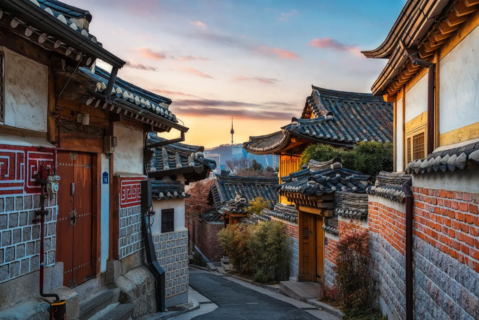 Bukchon Hanok Village alley with layered hanok rooftops and the modern Seoul skyline behind them