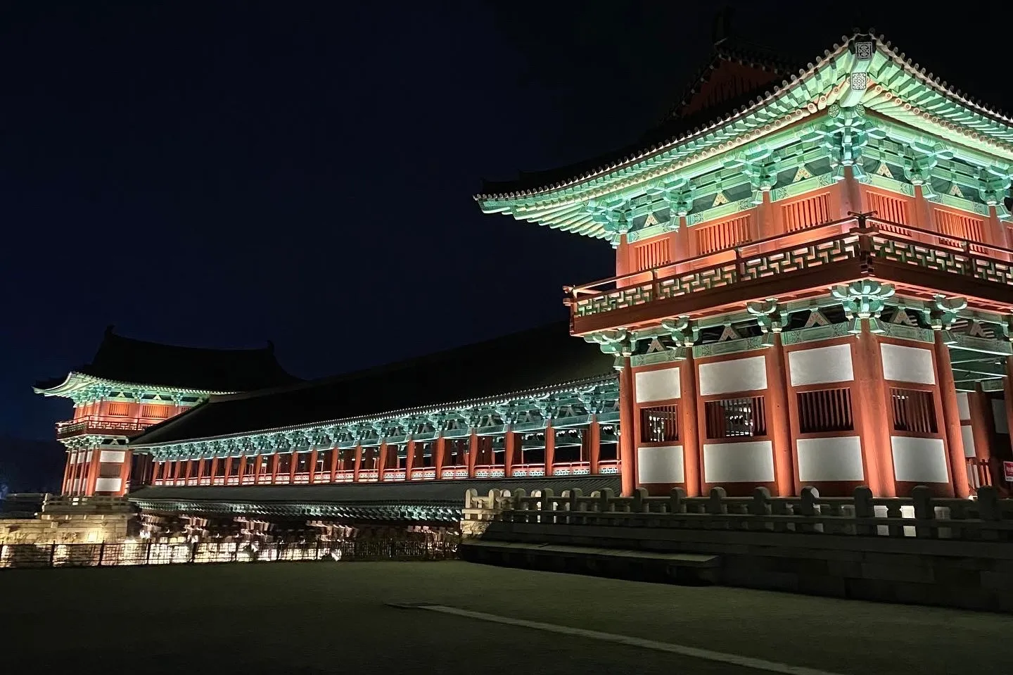 Woljeonggyo Bridge gatehouse at night, illuminated in warm red and green dancheong tones against a dark Gyeongju sky