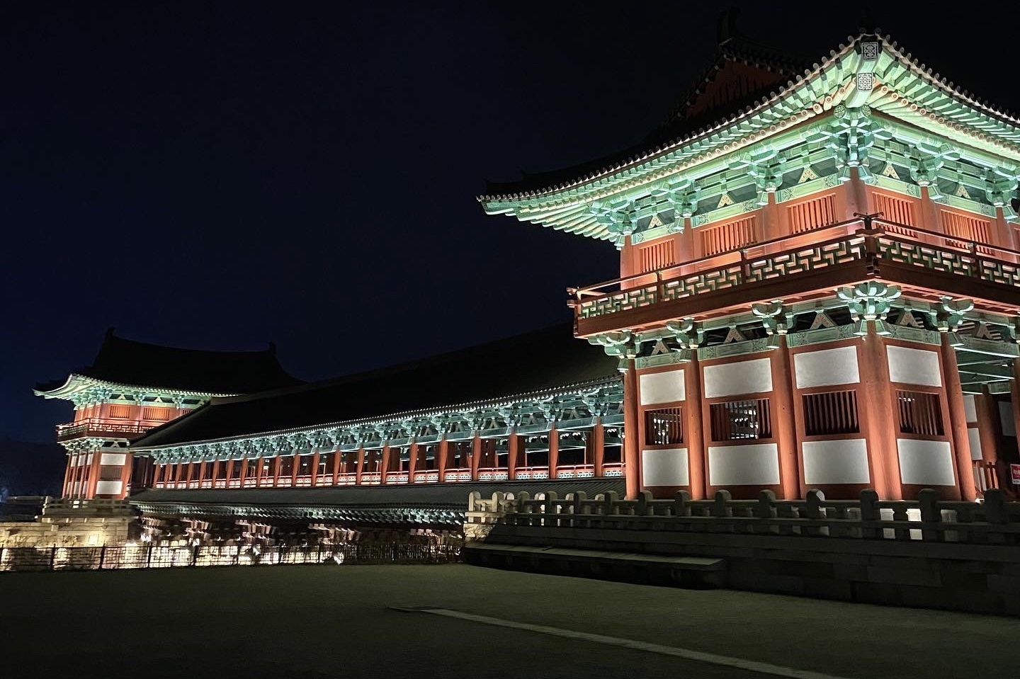 Woljeonggyo Bridge gatehouse at night, illuminated in warm red and green dancheong tones against a dark Gyeongju sky